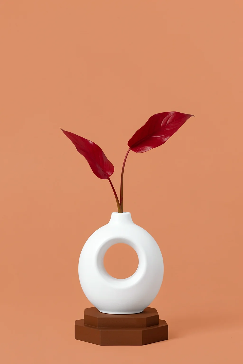 Abstract Botanical Vase. A white circular vase holding two dark-red leaves stands on a small brown plinth against a muted coral background.