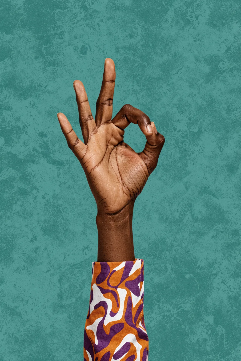 Okay. A dark-skinned hand makes an OK gesture against a textured teal background, emerging from a sleeve with a purple, orange, and white pattern.
