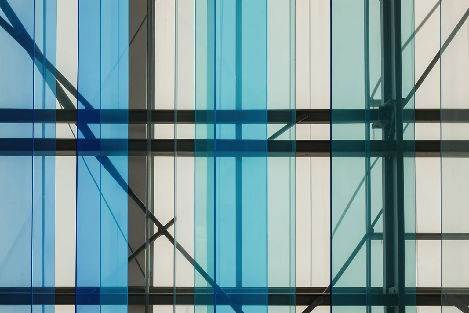 Blue Geometric Abstraction. Dark structural beams cross tall blue and turquoise glass panels in a geometric facade.