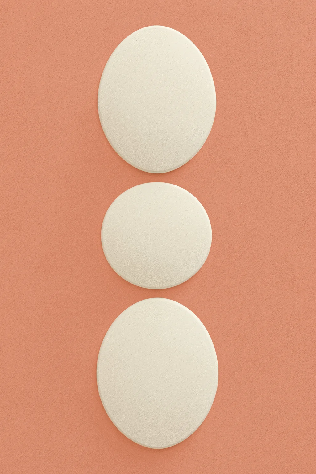 Earthy Stacked Vessels. Three raised ivory oval forms are stacked vertically on a muted coral background.