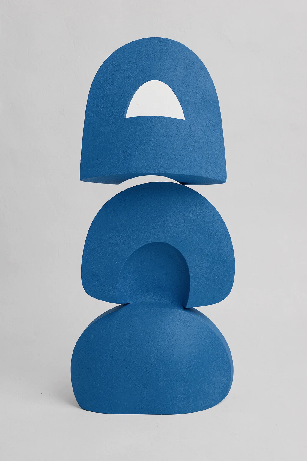 Abstract Blue Stack. Three sculptural blue forms, including an arch and rounded blocks, are stacked on a pale grey textured ground.