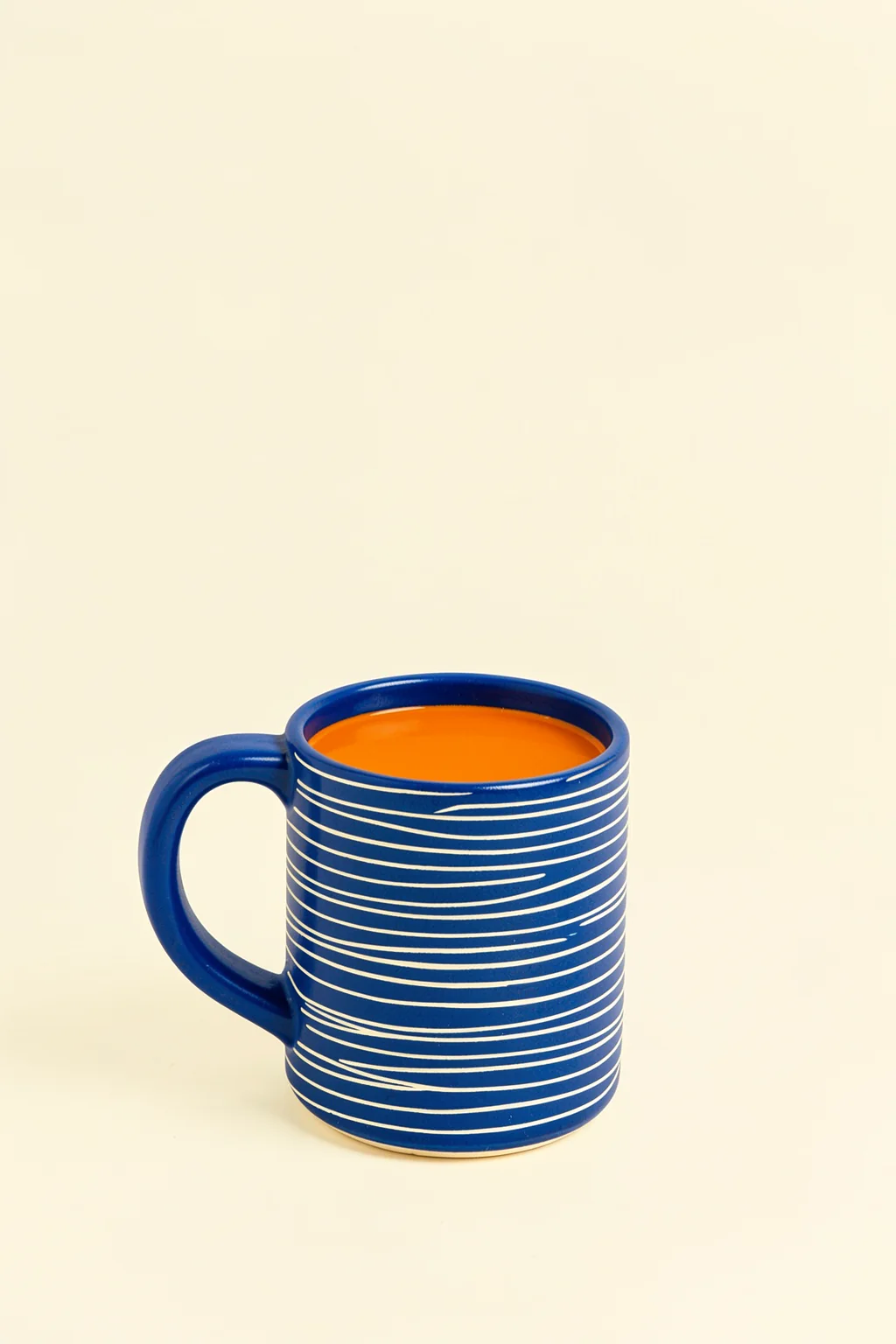 Blue Mug Moment. A blue mug with thin white stripes, filled with orange liquid, sits against a pale cream background.