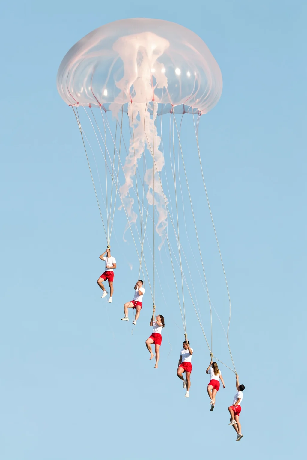 We came home smiling. Six people hang from fine lines beneath a large translucent jellyfish-shaped canopy in a pale blue sky.