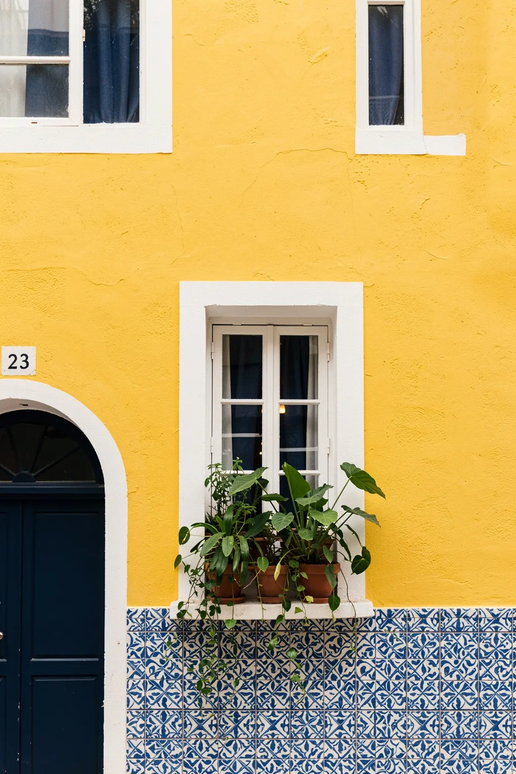 Bright Urban Balcony. A bright urban facade combines yellow stucco, a dark blue doorway, white windows, patterned blue tiles and potted greenery.