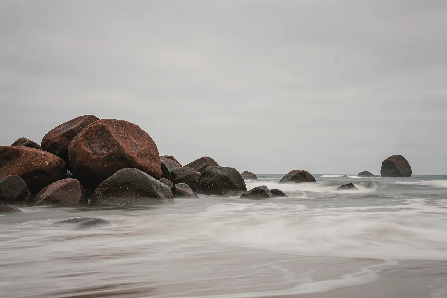 Smooth Ocean Rocks. Low rocks emerge from the sea beneath a soft grey sky as small waves break along the shoreline.