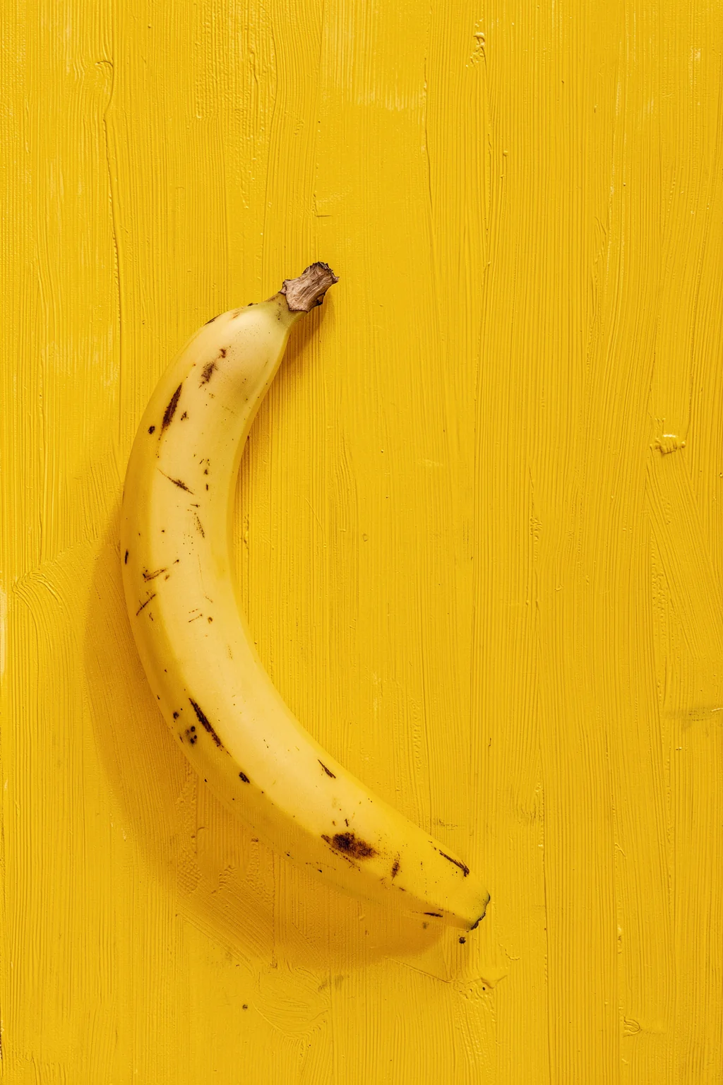 Golden Yellow Banana. A ripe yellow banana lies against a vivid yellow, brush-textured background.