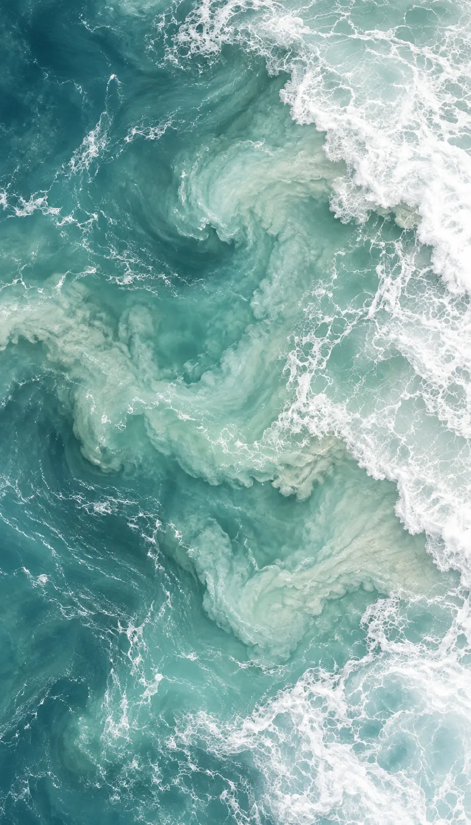 Aerial view of turquoise sea swirling into white foam along the shoreline.
