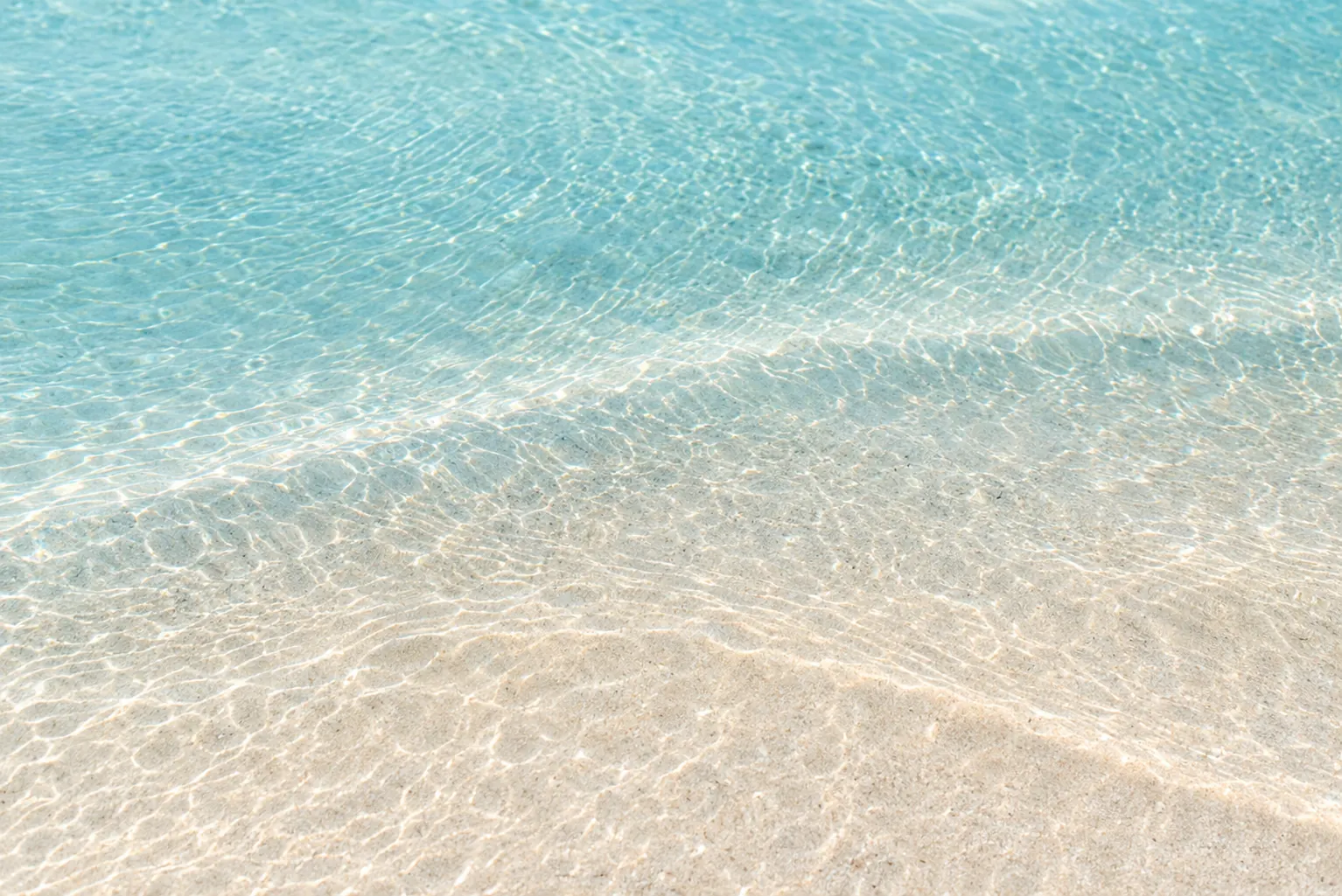 Clear turquoise shallows glide over pale sand in soft, rippled light.