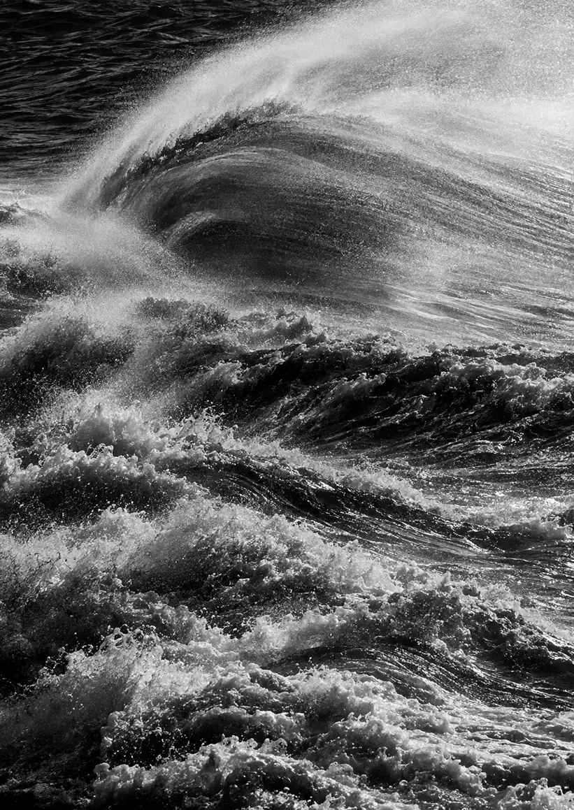 Black-and-white photo of a wave curling in a cloud of spray with fine detail in the water.
