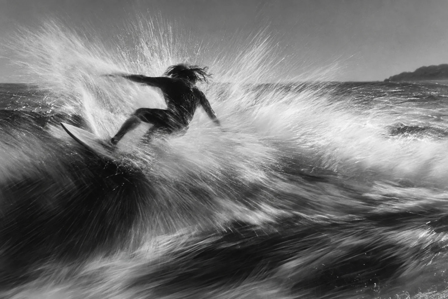 Black-and-white photo of a surfer carving through a wave, with spray and motion blur filling the frame.
