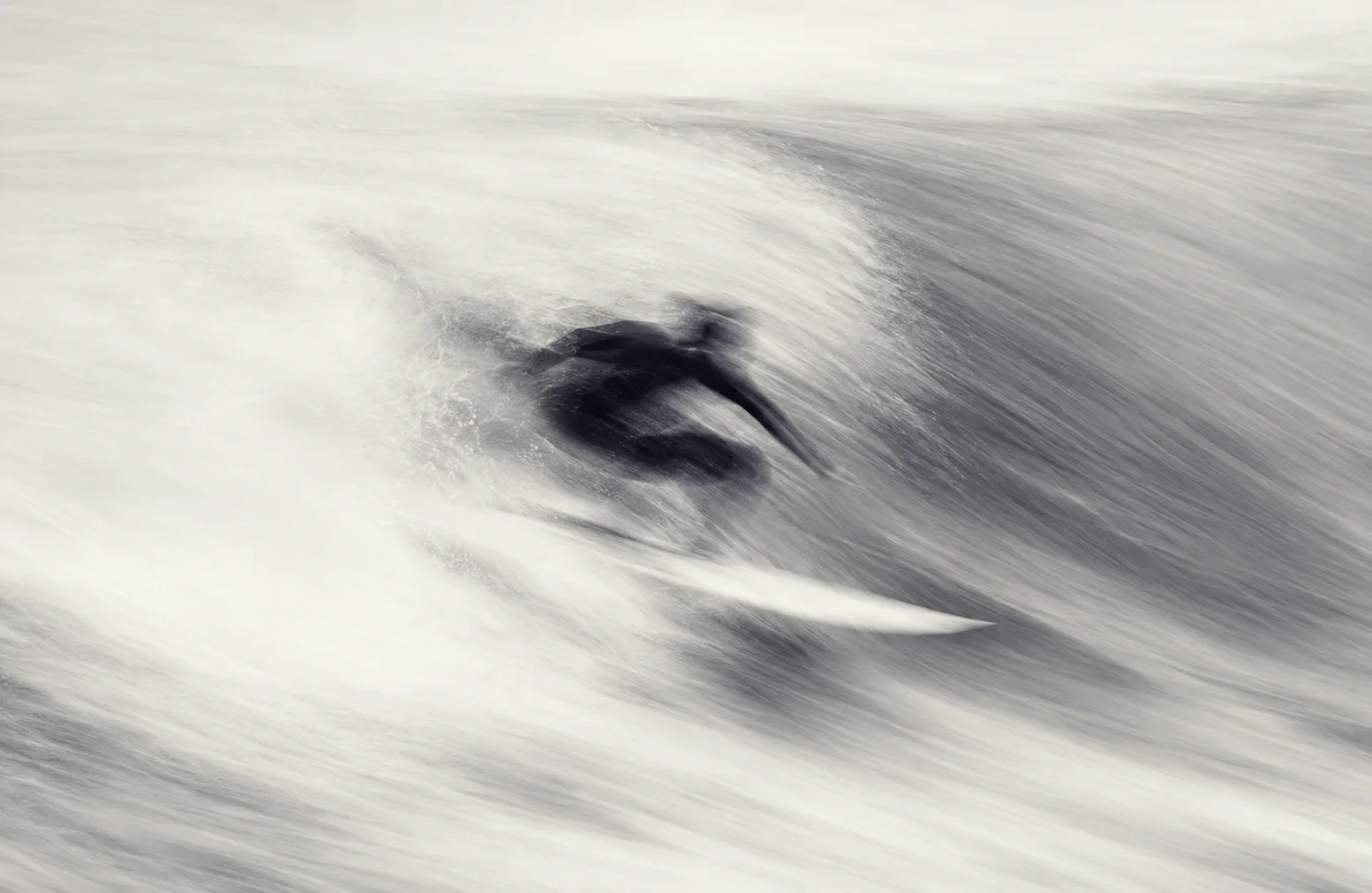 Black-and-white long-exposure photo of a surfer moving through a wave, with the form dissolved into soft streaks.