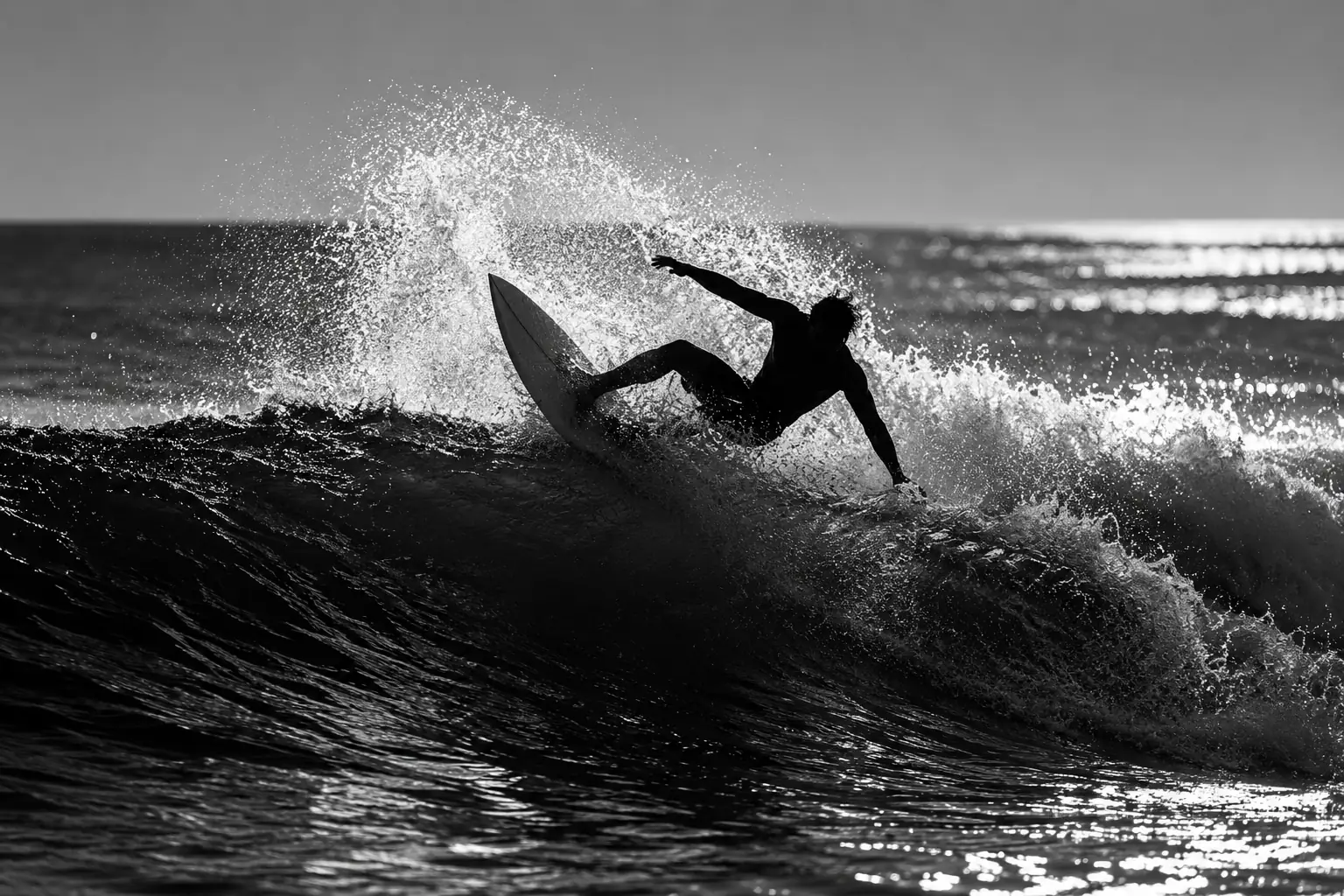 Black-and-white photo of a surfer carving a wave, with dark silhouettes and bright spray.