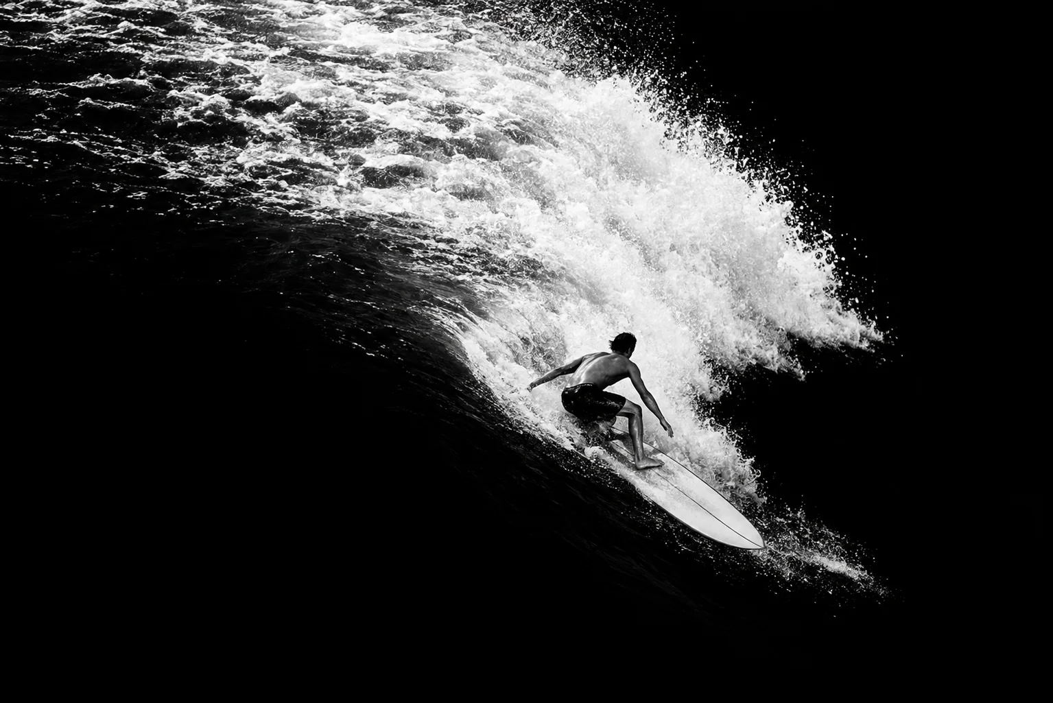 Black-and-white photo of a surfer inside a dark wave tube, with bright foam spilling from the lip.
