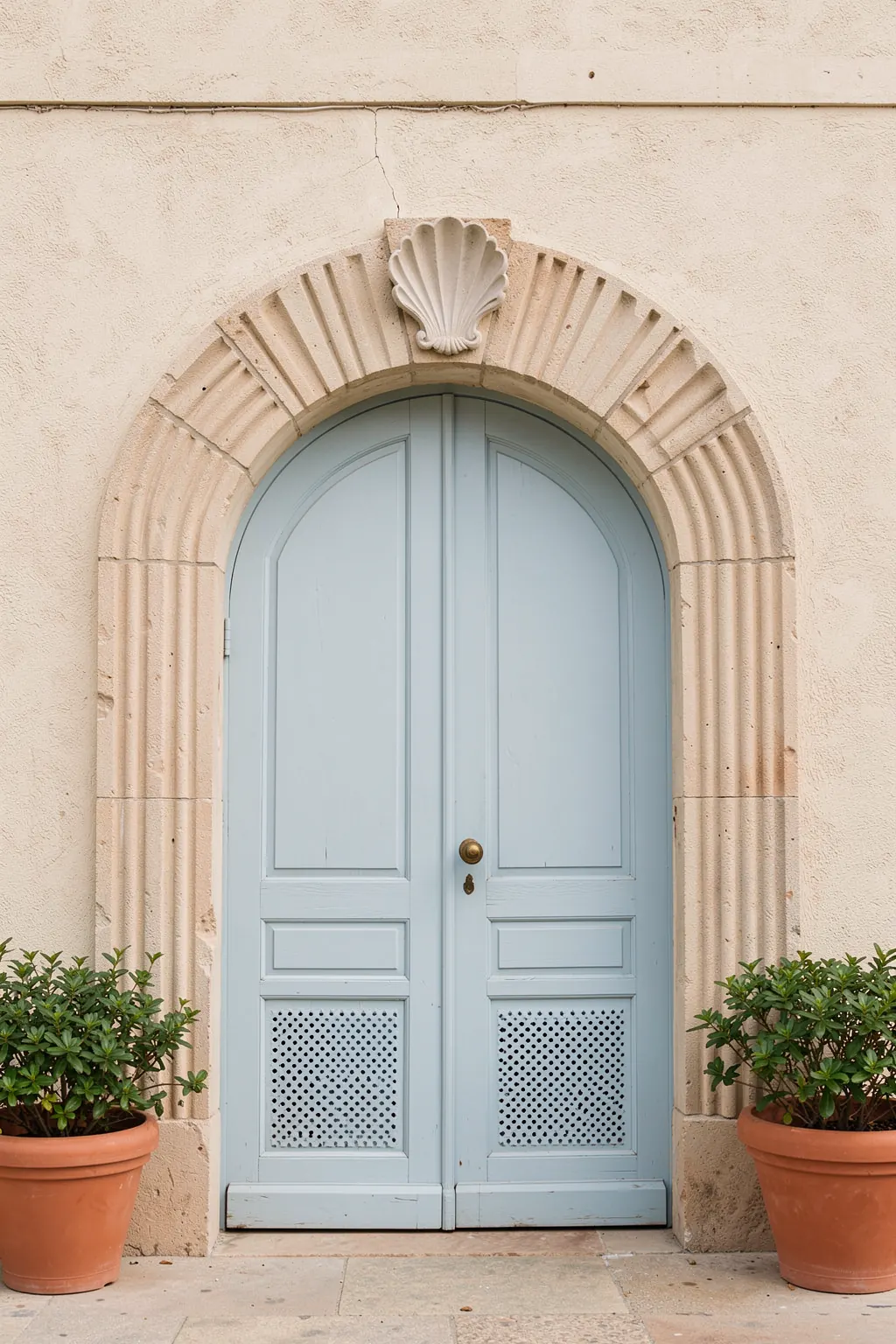 Blue tones of Rome - Italy travel photography. A pale stone arched doorway with a blue-gray door is framed by potted plants and greenery on a sunlit facade.