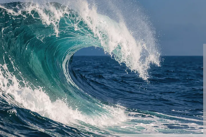 Crashing Turquoise Wave. A curling turquoise wave breaks into white foam above deep-blue ocean water.