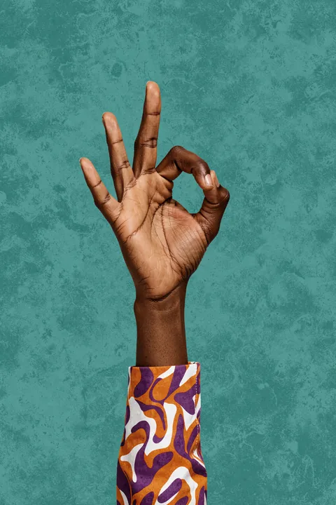 Okay. A dark-skinned hand makes an OK gesture against a textured teal background, emerging from a sleeve with a purple, orange, and white pattern.