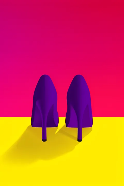 Confident High Heels. Two purple high-heeled shoes stand on a yellow surface against a bright magenta-pink background.