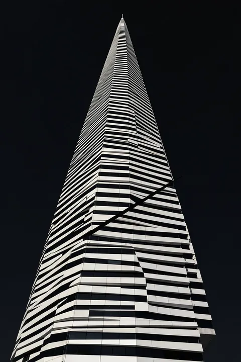 Modern Architectural Curves. A tall modern tower with alternating black-and-white horizontal bands rises into a dark sky, viewed from below.