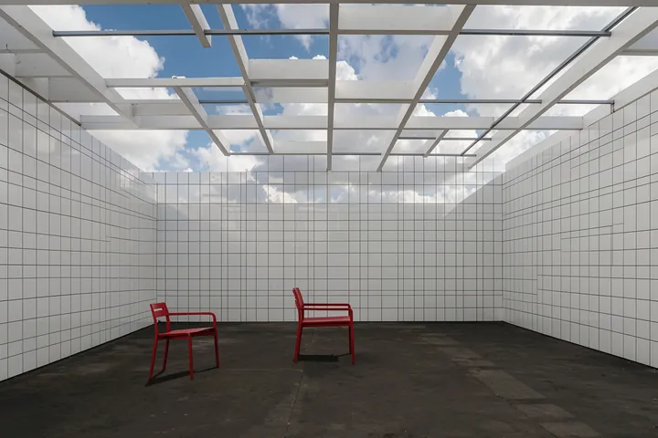 Red Chair on Rooftop. Two red chairs sit in a sparse tiled room beneath a glass roof with blue sky visible overhead.
