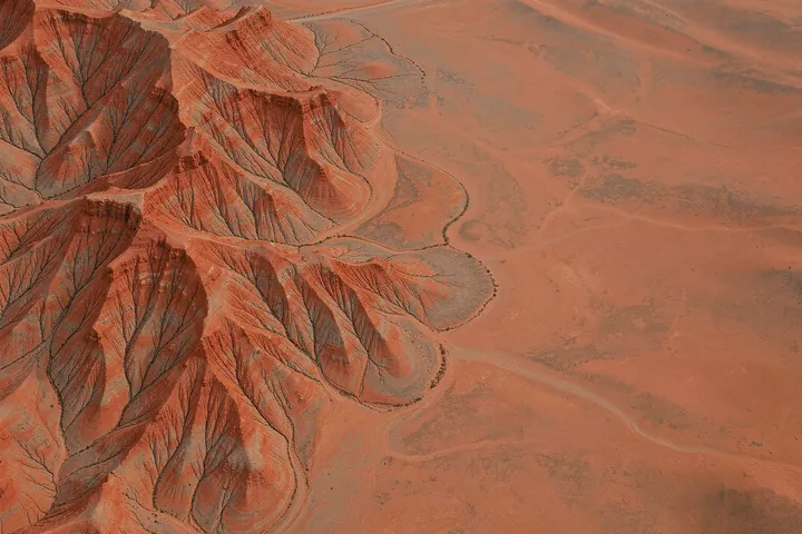 Rugged Desert Landscape. An aerial view of rust-red desert ridges and branching dry channels fills the image, with smoother open ground on the right.