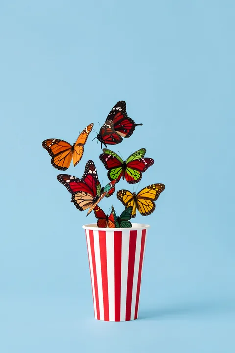 Whimsical Butterfly Pop. Brightly colored butterflies rise from a red-and-white striped cup against a pale blue background.