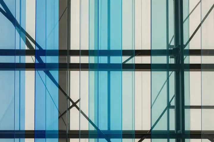 Blue Geometric Abstraction. Dark structural beams cross tall blue and turquoise glass panels in a geometric facade.