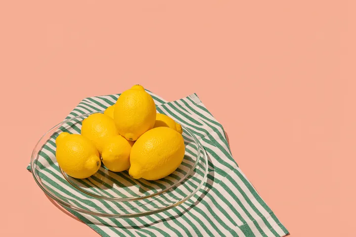 Lemons and stripes. Bright yellow lemons are piled on a plate over green-and-white striped cloth against a peach background.