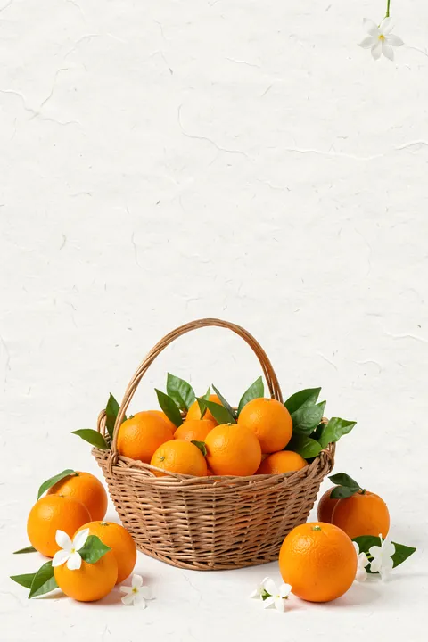 Sweet Orange Blossoms. A wicker basket filled with oranges and green leaves sits with loose oranges and white blossoms on textured cream.