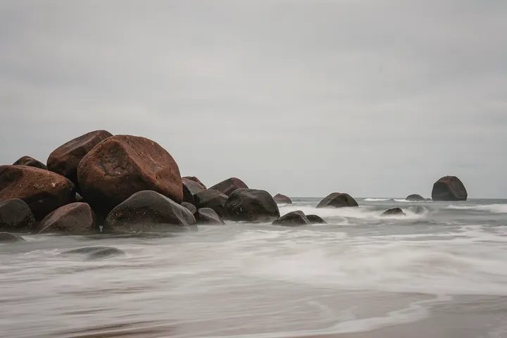 Smooth Ocean Rocks. Low rocks emerge from the sea beneath a soft grey sky as small waves break along the shoreline.