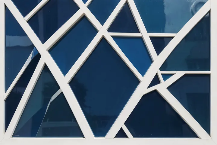 Geometric Blue Facade. White intersecting geometric mullions divide deep blue reflective glass across a close-up building facade.