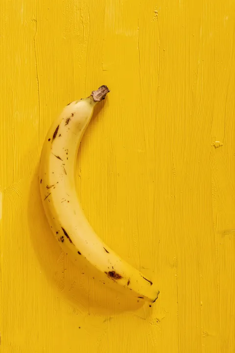 Golden Yellow Banana. A ripe yellow banana lies against a vivid yellow, brush-textured background.