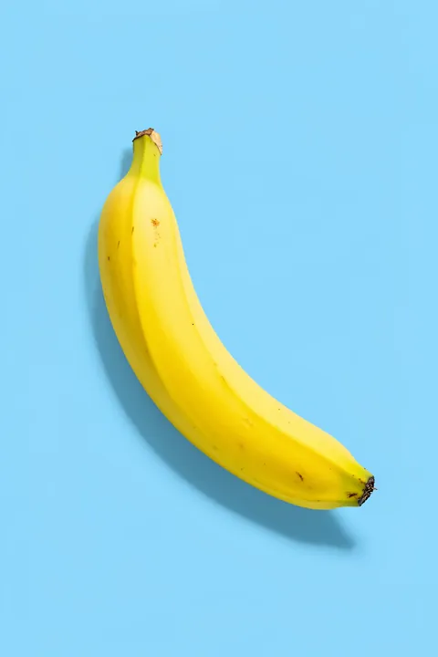 Bold Banana Statement. A single bright yellow banana floats diagonally against a clear sky-blue background.