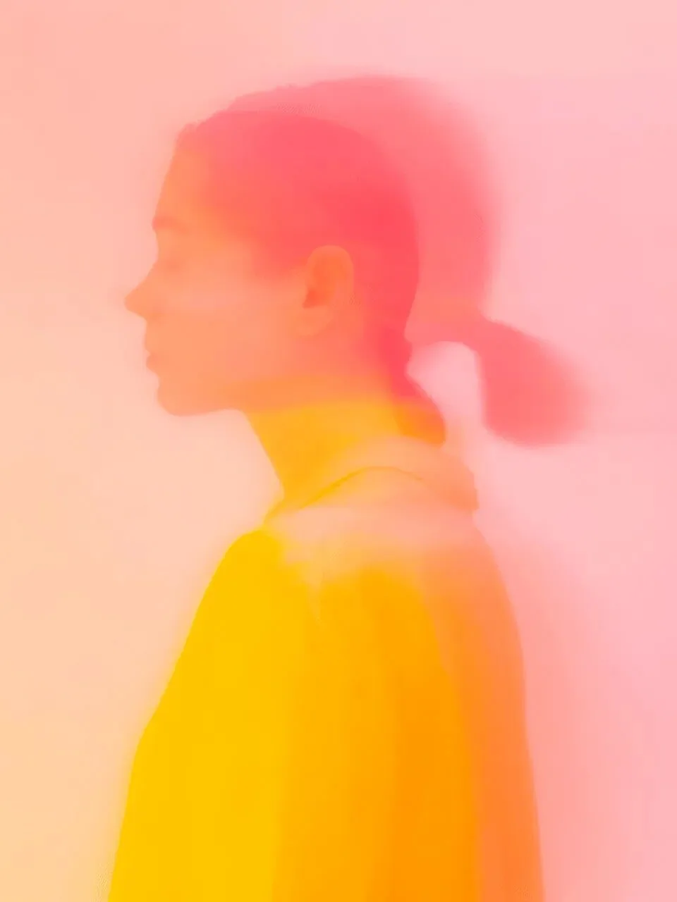 Onlly poster, Woman in Golden Light: A softly blurred profile glows in coral, pink and yellow tones.