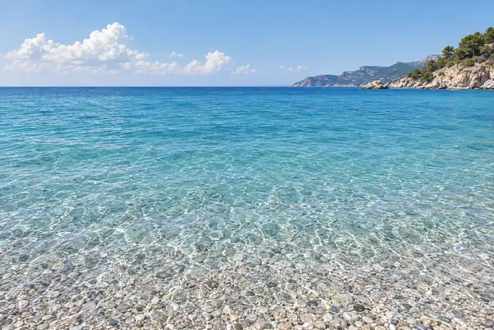 Clear turquoise sea runs toward a green headland under a sky with a few clouds.