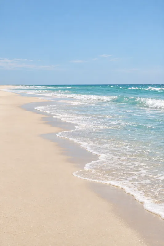 Turquoise waves break in white foam along a long, pale sandy beach.