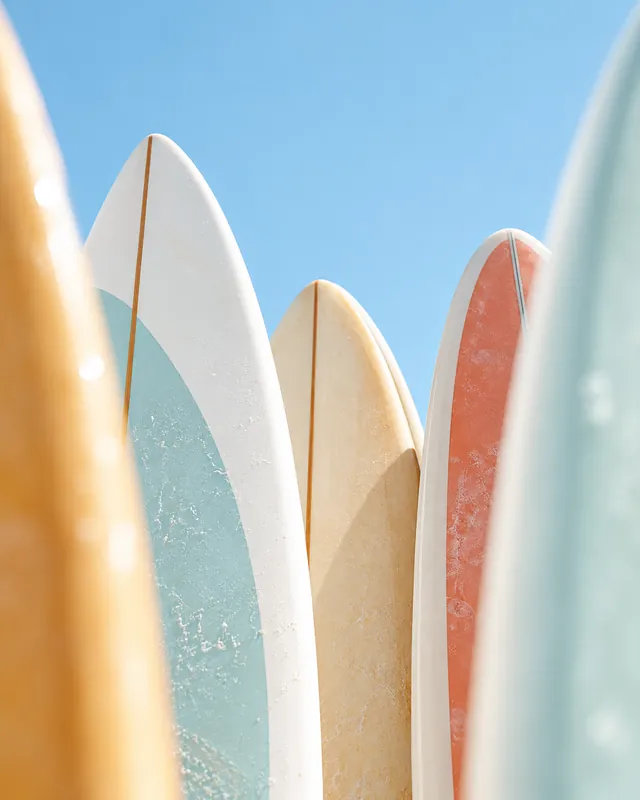 Close-up of colourful surfboards in yellow, mint, cream and coral standing against a pale blue sky.