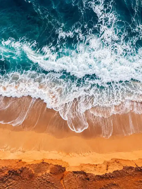 Aerial view of turquoise waves sweeping over warm orange sand, with white foam curling in long lines.